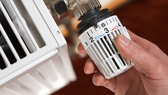 Ingo Bartussek - stock.adobe.com Hand an Thermostat einer Heizung